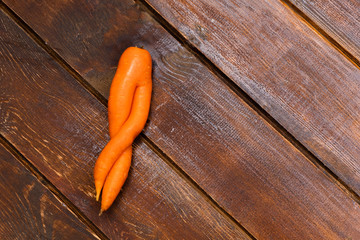 Ugly twisted carrot on wooden background. Image with copy space, top view.