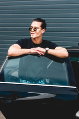 handsome stylish man in sunglasses posing near car and looking away