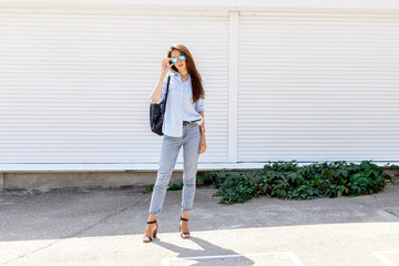 Young stylish woman wearing blue shirt, blue cropped denim jeans, black high heel sandals, black...