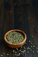 Dried green peppercorns in a wooden bowl. Dark wooden table, high resolution, negative space