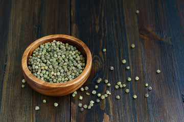 Dried green peppercorns in a wooden bowl. Dark wooden table, high resolution