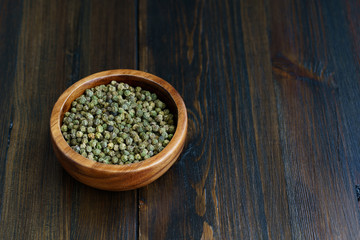 Dried green peppercorns in a wooden bowl. Dark wooden table, high resolution, negative space