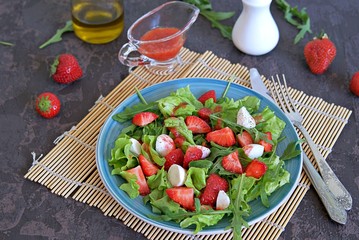 Salad with strawberries, arugula and mozzarella cheese on a dark brown background concrete. Healthy food.
