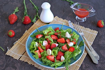 Salad with strawberries, arugula and mozzarella cheese on a dark brown background concrete. Healthy food.