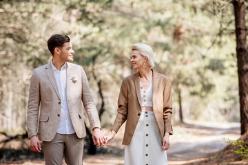 Fototapeta premium happy stylish couple holding hands and looking at each other in forest