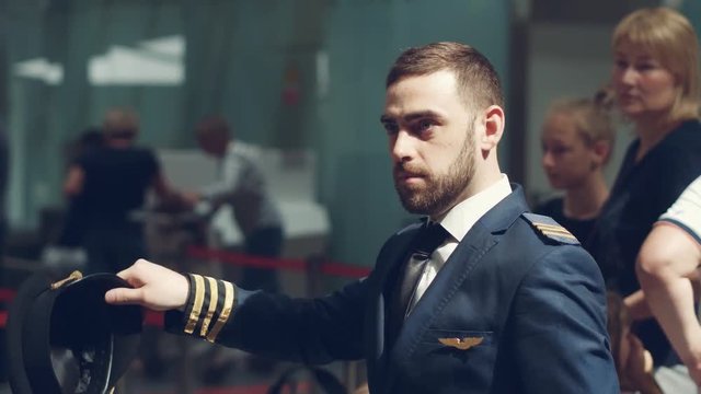 Portrait of a Pilot in uniform with golden stripes and cap . He is standing in the terminal of an airport.