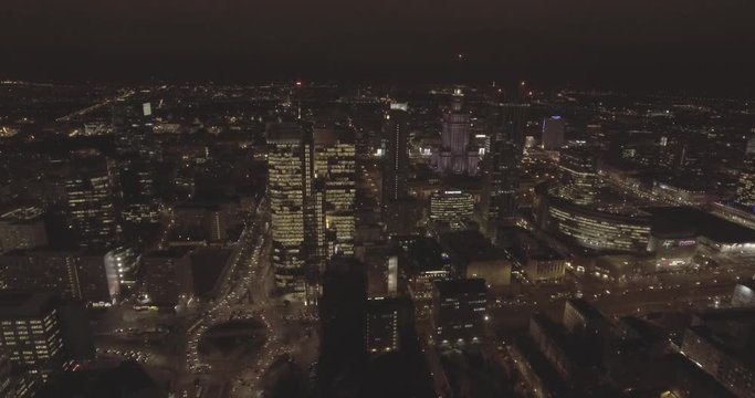 4K. AERIAL VIEW. Flying over the rooftops of skyscrapers, office buildings and apartment buildings in the center of Warsaw at night. with bright night lighting. 4K. Drone shot RAW.