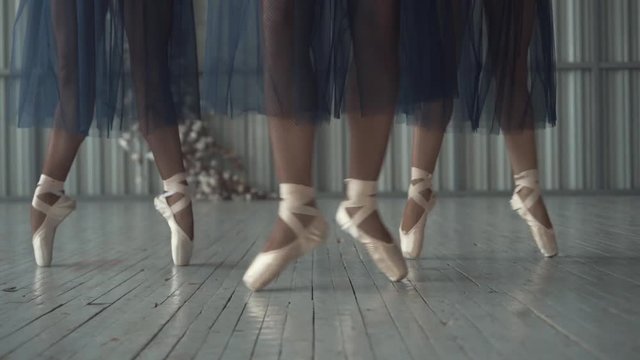 Close-up of ballet dancers legs in pointe shoes, tights and mesh skirt training in the choreography room on the wooden floor. Action. Ballet classes