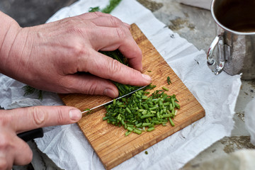 Person cut herbs on wooden board with knife