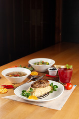 Diet, but nutritious lunch in a restaurant, served on a wooden table: pork patty with boiled bulgur, hot soup with meatballs and vegan pasta with olives  as a nutritious lunch in a cafe