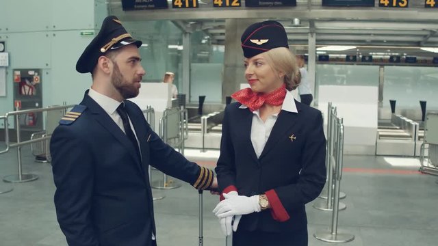 Handsome male pilot and attractive female flight attendant are standing in airport terminal together.