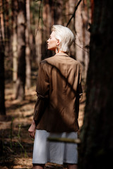Fototapeta premium pensive blonde woman in brown jacket standing in forest