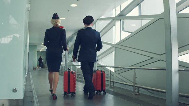 Pilot and stewardess with red suitcases walking by airport. Back view.