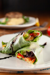 Yummy vegan spring rolls in a rice paper with carrot, greens, bell pepper and cucumber on a dark background