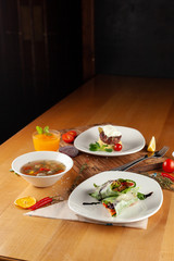 Steak with mashed potatoes, light vegetable soup with meatballs and vegetarian spring roll as a set meal, placed on a wooden table with sidelight