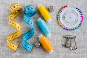 Fototapeta na wymiar sewing tools: colored threads for sewing, centimeter ribbons, thimbles and colored pins on a light gray background close-up
