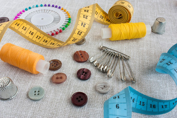 Fototapeta na wymiar sewing tools: colored sewing threads, several buttons, centimeter ribbons, thimbles and colored safety pins on a light gray background close-up
