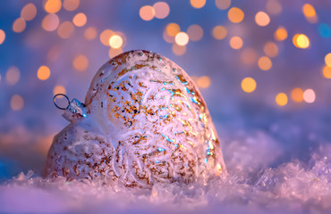 Glass heart on a snow and toned blurred color background of glittering bokeh with glowing lights....