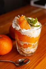 Layered tangerine dessert in a glass with whipped cream cheese, decorated with fresh mint on a wooden background