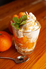 Layered tangerine dessert in a glass with whipped cream cheese, decorated with fresh mint on a wooden background