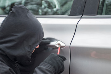 The man dressed in black with a hood on his head trying to break into the car. Car thief, car theft...