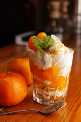 Healthy light tangerine dessert in a glass with whipped cream cheese, decorated with fresh mint on a wooden background