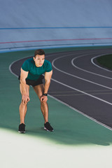 Obraz premium mixed race sportsman with hands on knees standing at stadium