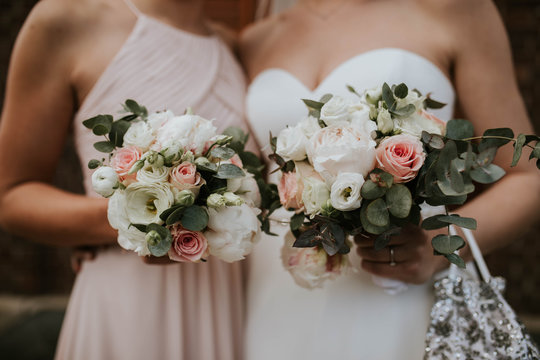 Midsection of bride and bridesmaid holding bouquet