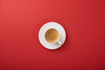 Top view of white cup with coffee on saucer on red background