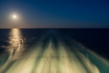 Moon rising over wake and waves of cruise ship at sea with concept of leaving or starting anew