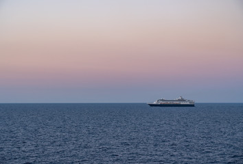 Small cruise liner sailing across the ocean as dawn starts to light the sky