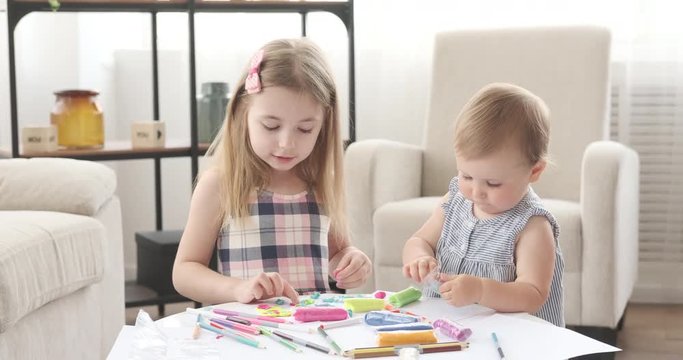 Baby girl with her sister enjoying playing with plasticine at home