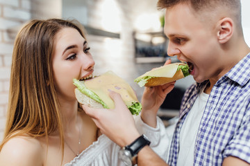 Husband reaching over his wife's shoulder to taste the sandwich which she is offering him. Family day.