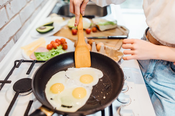 Portrait of woman will cracking an egg over a frying pan on stove. Female preparing breakfast omlette.