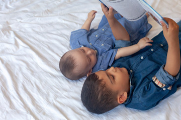 Two little brothers reading a book. Infant kids lying on the bed and read the tale before sleeping....