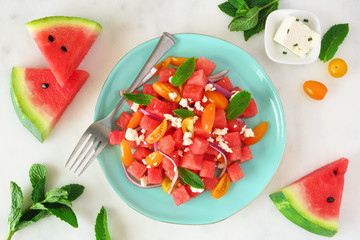 Watermelon and tomato salad with feta cheese. Overhead view on blue plate. Table scene with a...