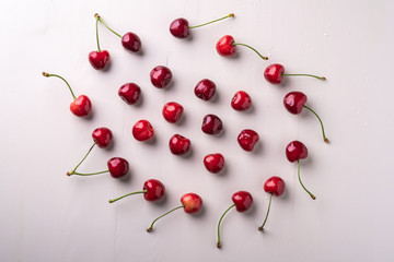 Obraz na płótnie Canvas Copy space circle of cherry berries with stem on wooden white background and water drops top view