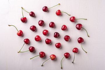 Obraz na płótnie Canvas Copy space circle of cherry berries with stem on wooden white background and water drops top view