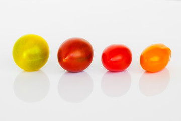 Close-up of yellow, brown, red and orange cherry tomatoes on a white glossy background. Mix of multicolored small and tasty tomatoes.