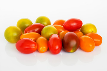 Mix of multicolored cherry tomatoes on a white glossy background. Heap of yellow, orange and red small tasty tomatoes. Vegetarian and healthy eating.