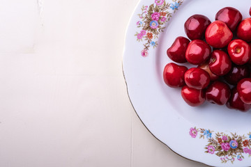 Cherry berries in white plate texture on wooden white background top view