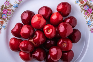 Cherry berries in white plate texture on wooden white background top view