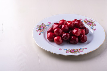 Cherry berries in white plate texture on wooden white background angle view