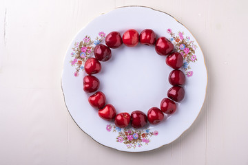 Circle of cherry berries in white plate texture on wooden white background top view