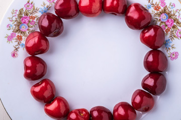 Circle of cherry berries in white plate texture on wooden white background top view