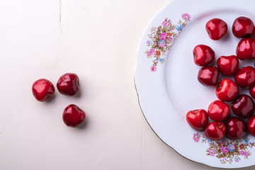 Cherry berries in white plate texture on wooden white background top view