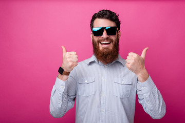 Naklejka premium Portrait of young bearded man in casual showing thumbs up gesture and smiling