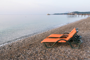 Fototapeta na wymiar Plastic sun beds with orange capes on the sea beach at sunrise. Summer vacation concept.