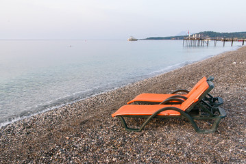Plastic sun beds with orange capes on the sea beach at sunrise. Summer vacation concept.