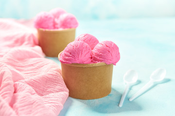 two portions strawberry ice cream in paper cup and pink napkin on mint colors background, selective focus